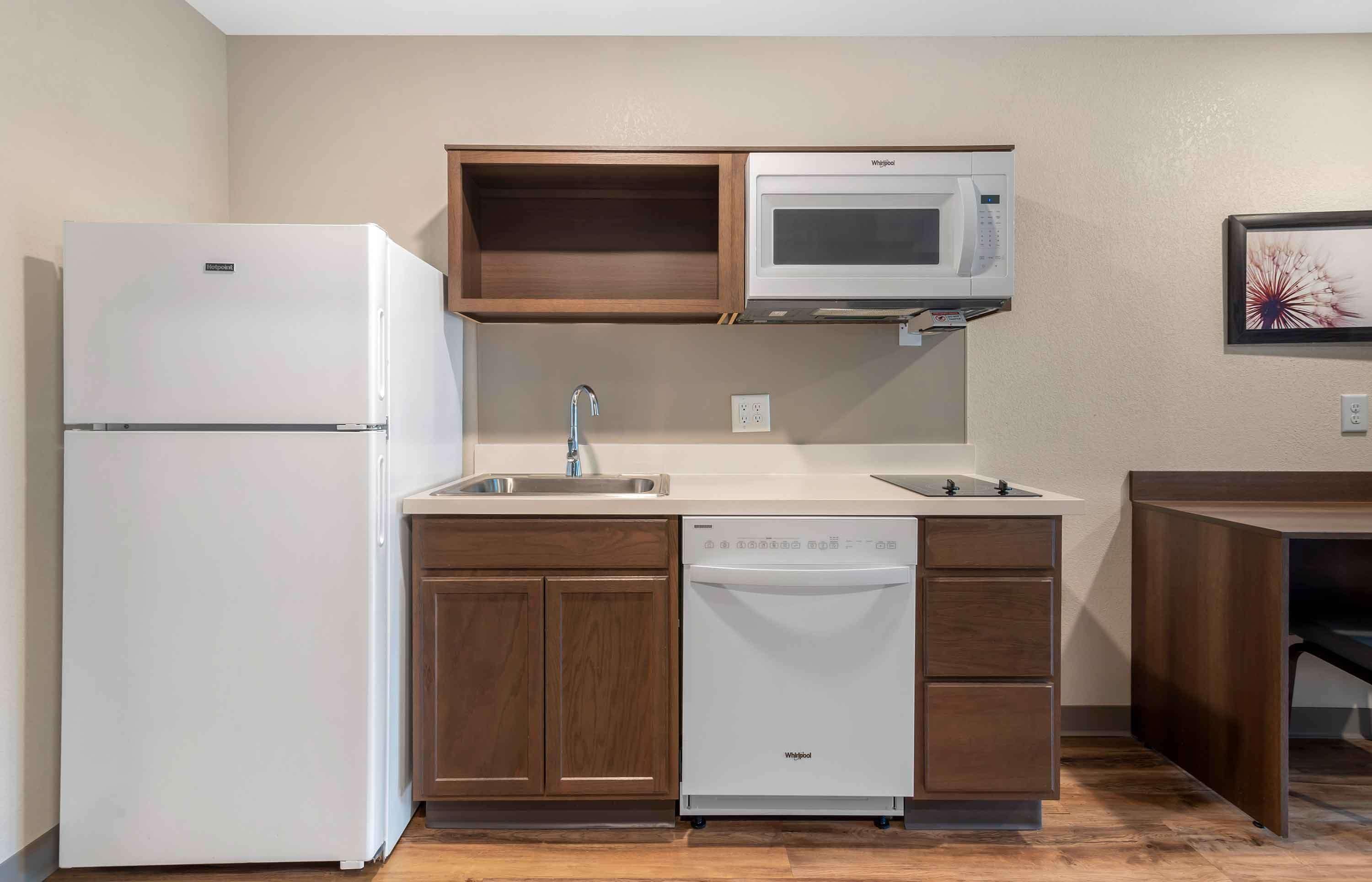 A compact kitchen with a refrigerator, microwave, dishwasher, and wooden cabinets.