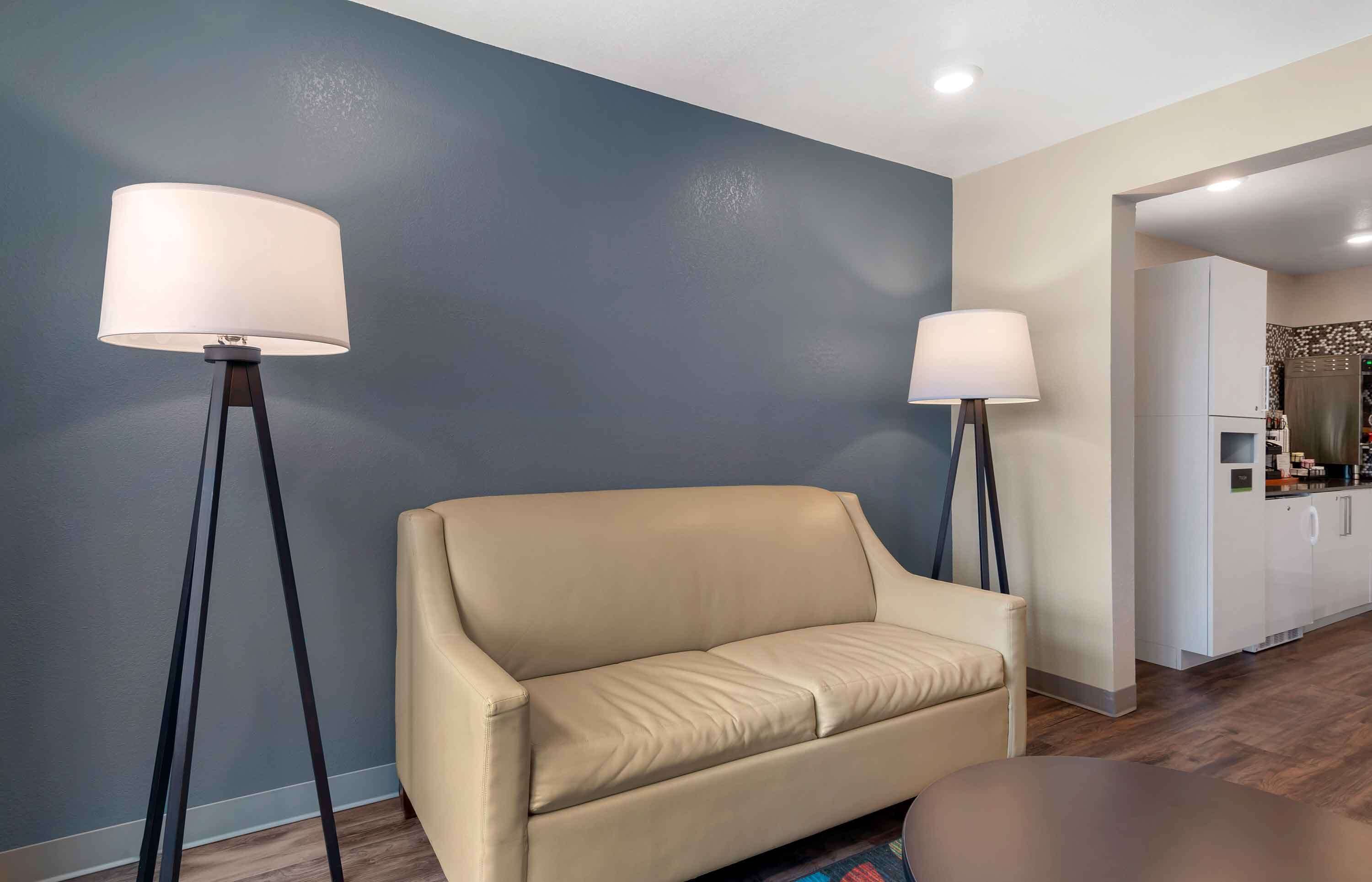 Una sala de estar moderna con un sofá color crema, dos lámparas de pie y una cocina al fondo.