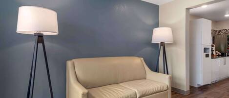 Una sala de estar moderna con un sofá color crema, dos lámparas de pie y una cocina al fondo.