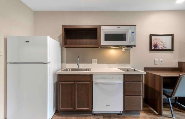 Cocina compacta con refrigerador, microondas, lavavajillas y armarios de madera.