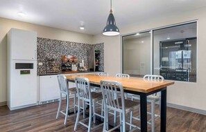 Una cocina moderna con una mesa de comedor de madera, sillas blancas y una lámpara colgante negra.