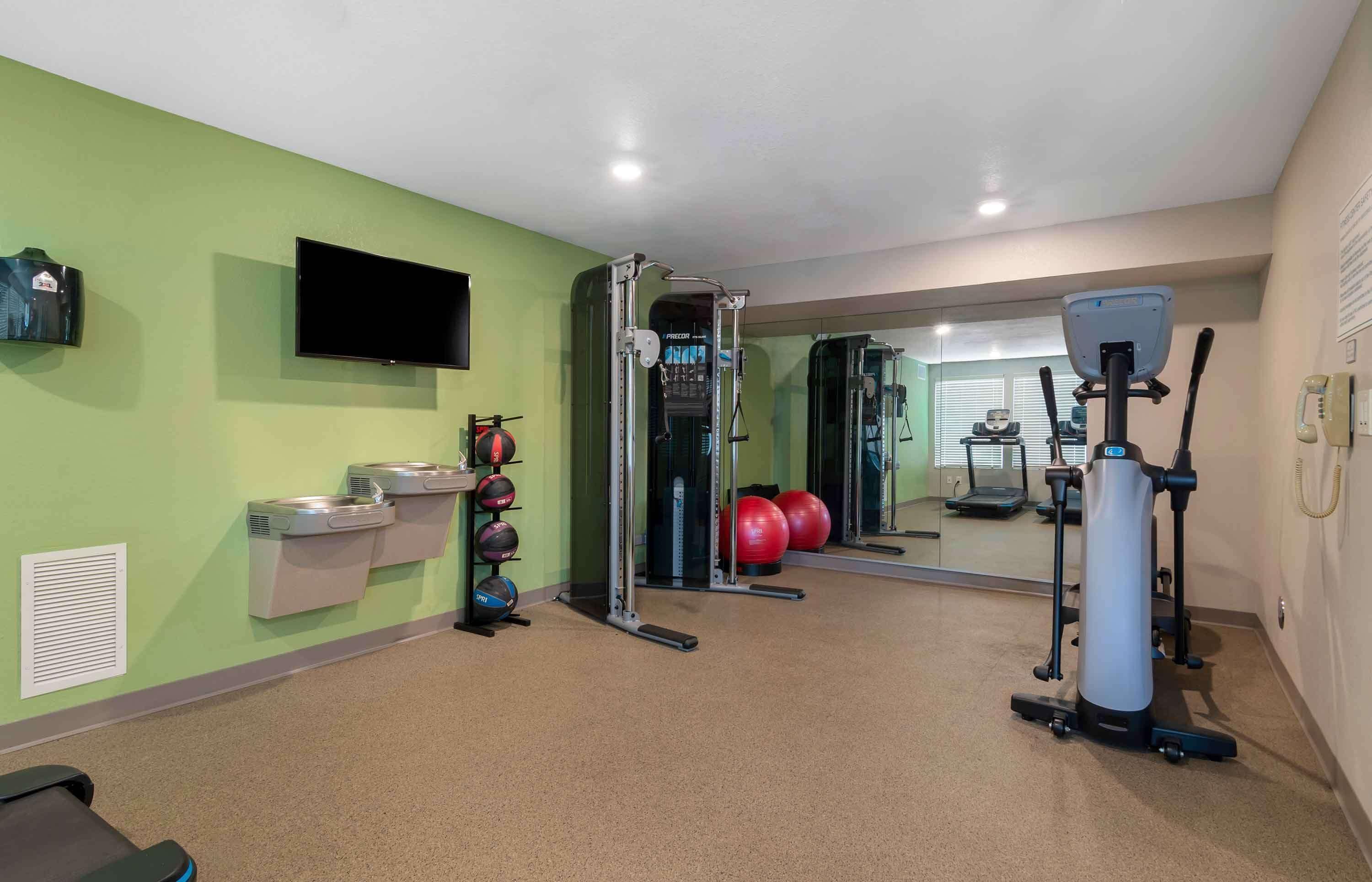 Un gimnasio con equipo de ejercicio, una televisión y un espejo.