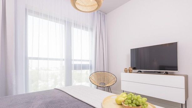 Un dormitorio moderno con cama, televisor, una silla de mimbre y un frutero en la mesita de noche.