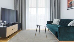 A modern living room with a flat-screen TV, a dark sofa, a small round table, and a patterned rug. - Novis Apartments Przy Rotundzie (Warsaw)
