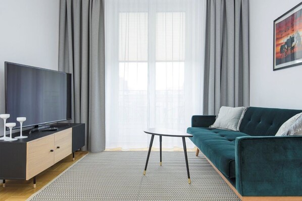 A modern living room with a flat-screen TV, a dark sofa, a small round table, and a patterned rug.