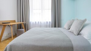 A bedroom with a bed, a desk, and a window with curtains. - Novis Apartments Przy Rotundzie (Warsaw)