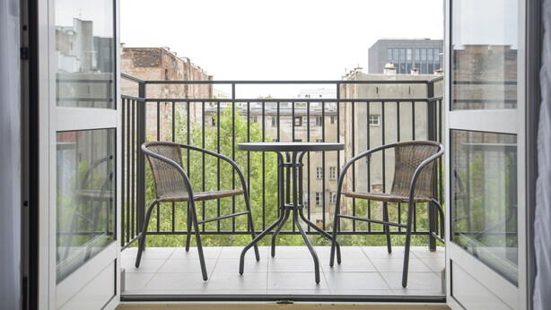 A balcony with two wicker chairs and a small table, overlooking a cityscape with buildings and greenery. - Novis Apartments Przy Rotundzie (Warsaw)