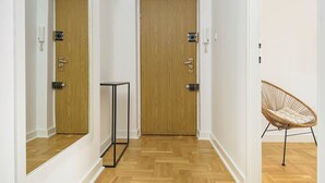 A hallway with two wooden doors, a small table, and a wicker chair. - Novis Apartments Przy Rotundzie (Warsaw)
