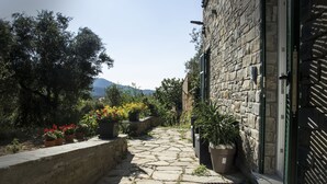 A stone pathway leading to a stone building with a door, surrounded by potted plants and flowers. - The Garden (Riomaggiore)