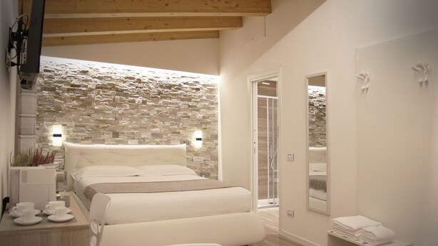 A modern bedroom with a stone wall, a bed, a desk with cups, and a mirror. - The Garden (Riomaggiore)