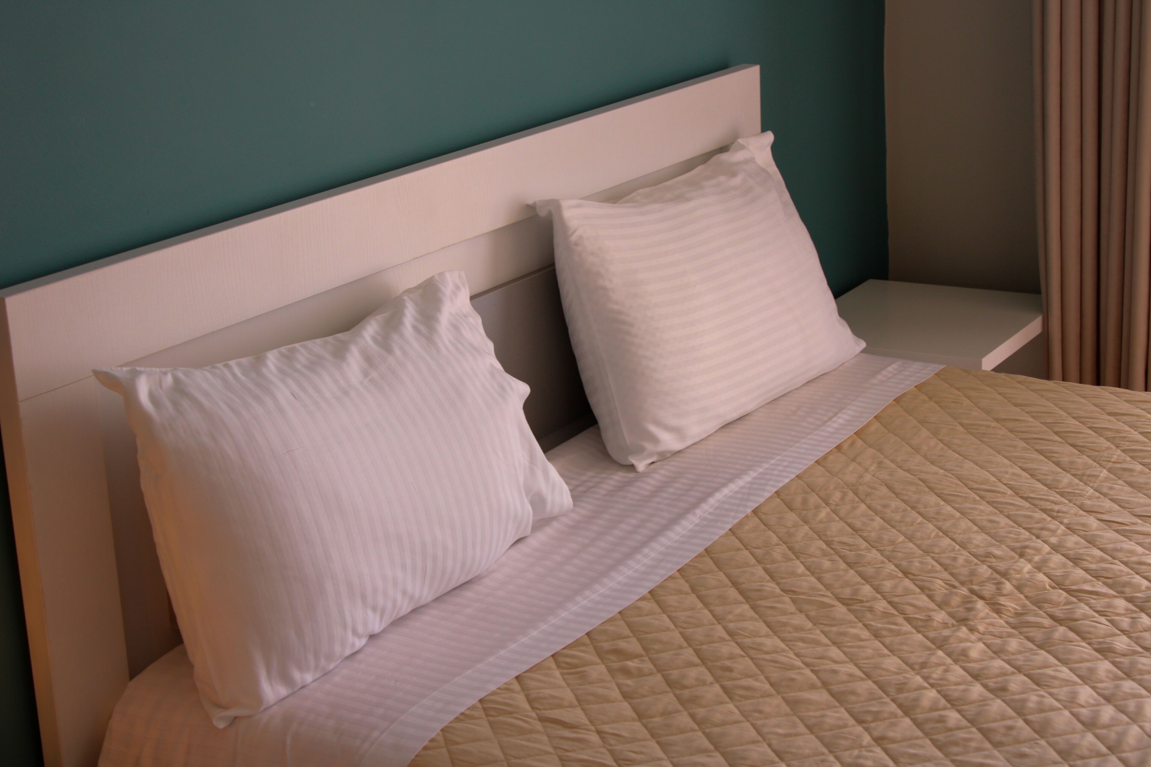 A bed with white pillows and a beige quilted bedspread in a room with teal walls.