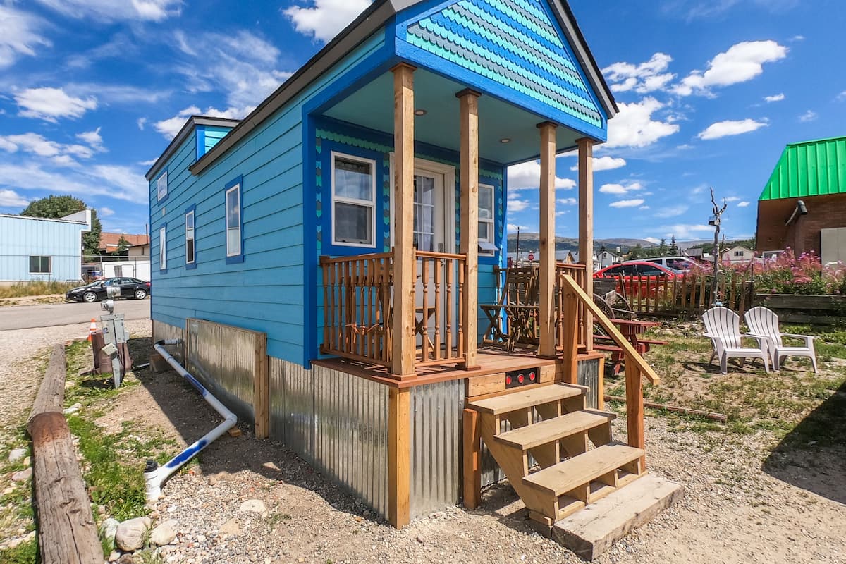 Une maison bleue avec un porche en bois et des marches menant à une terrasse.