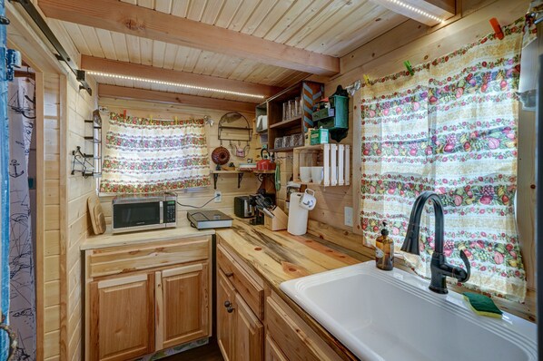 Una cocina de madera con microondas, pileta y diferentes utensilios.