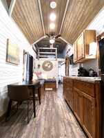 Una cocina con gabinetes de madera, un comedor con mesa y sillas, y un ventilador de techo.