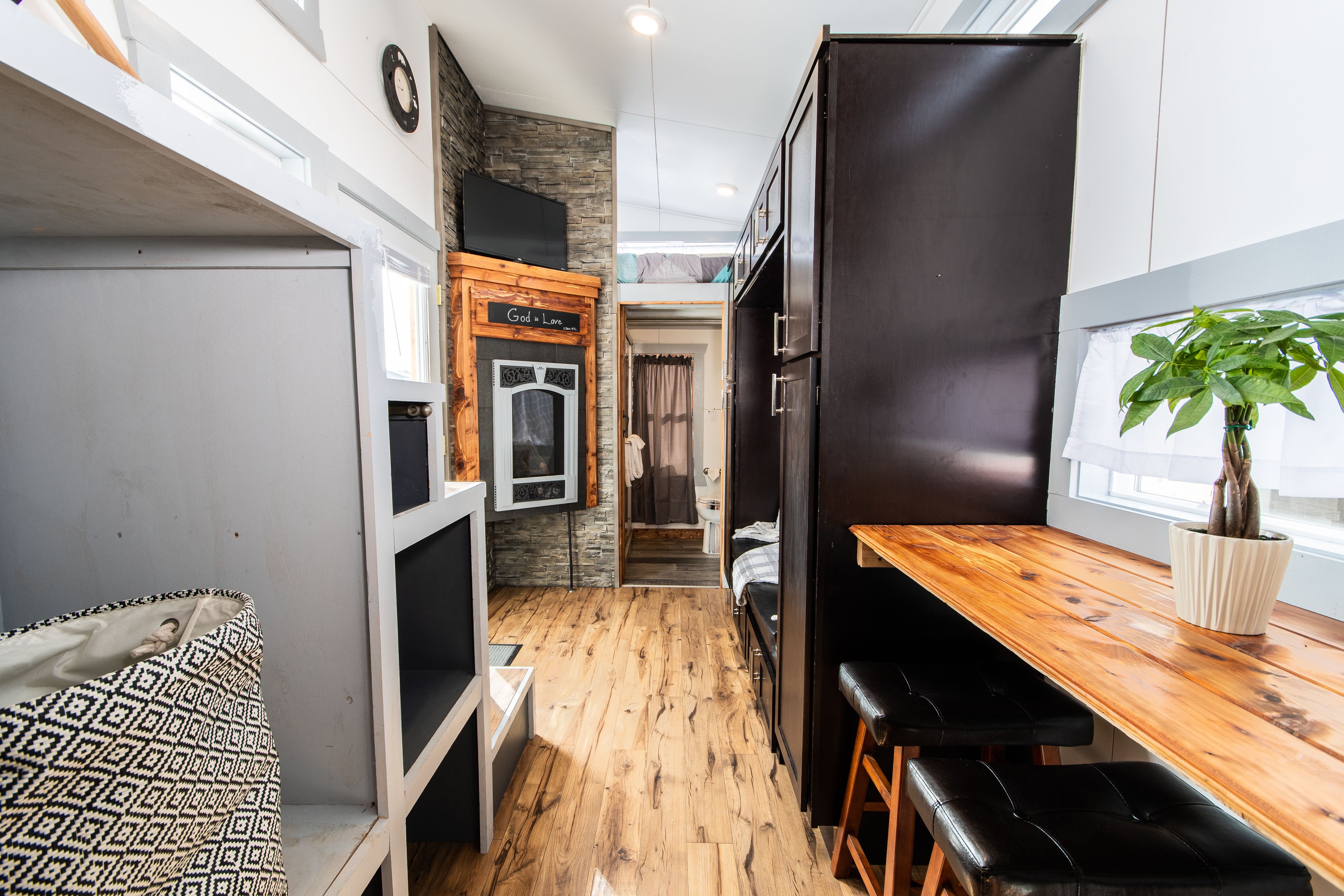 A narrow hallway with a wooden floor, a bench, a table with a plant, and a door leading to another room.