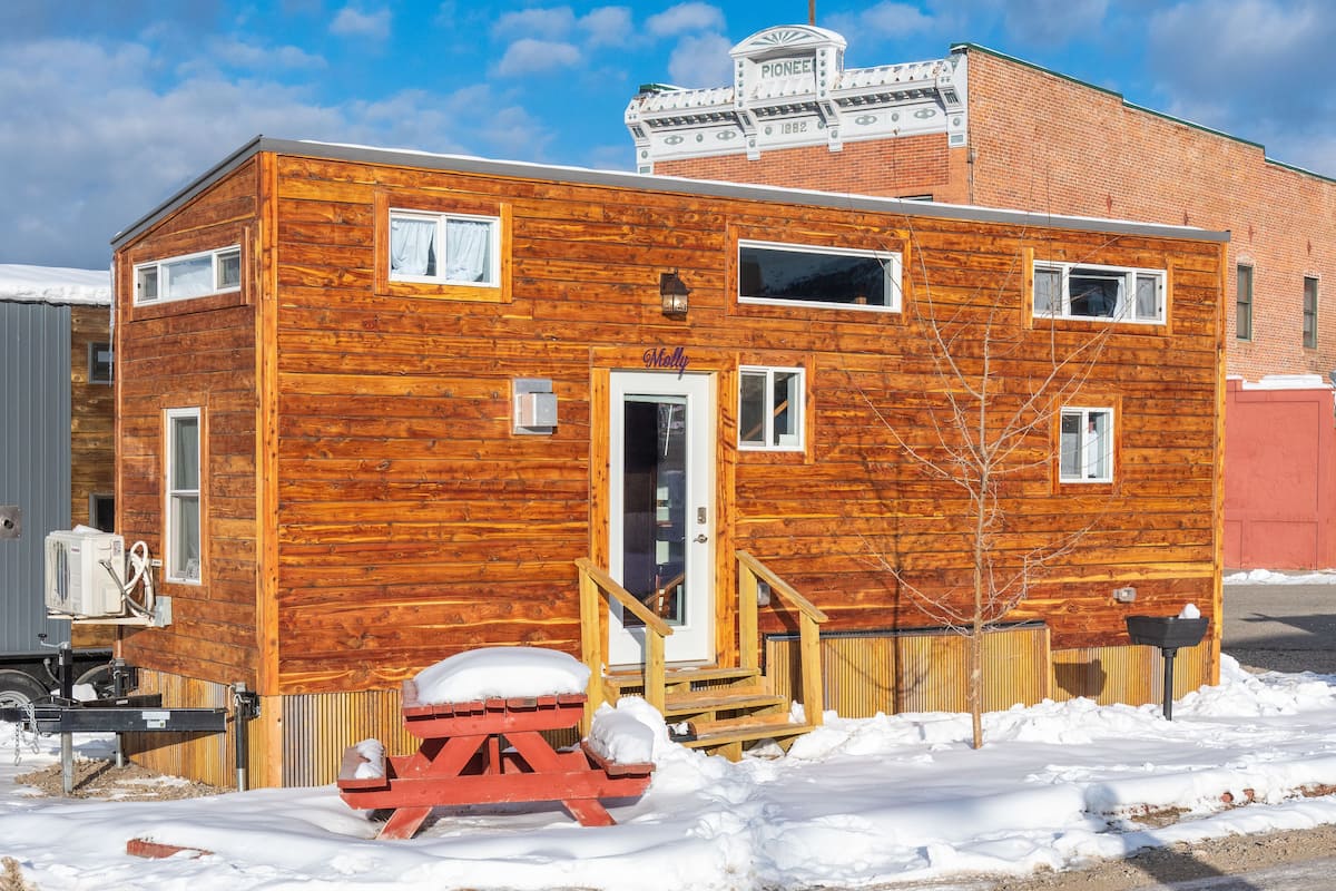 Une cabane en bois avec une porte d’entrée, des fenêtres et un petit porche.