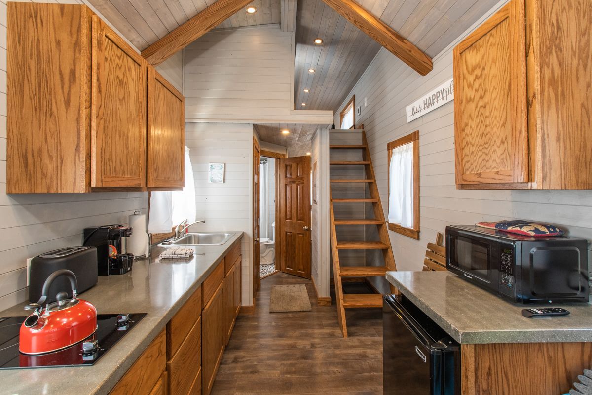 A kitchen with wooden cabinets, a red kettle, a microwave, and a ladder leading to a loft bedroom.