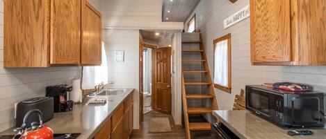 A kitchen with wooden cabinets, a red kettle, a microwave, and a ladder leading to a loft bedroom.