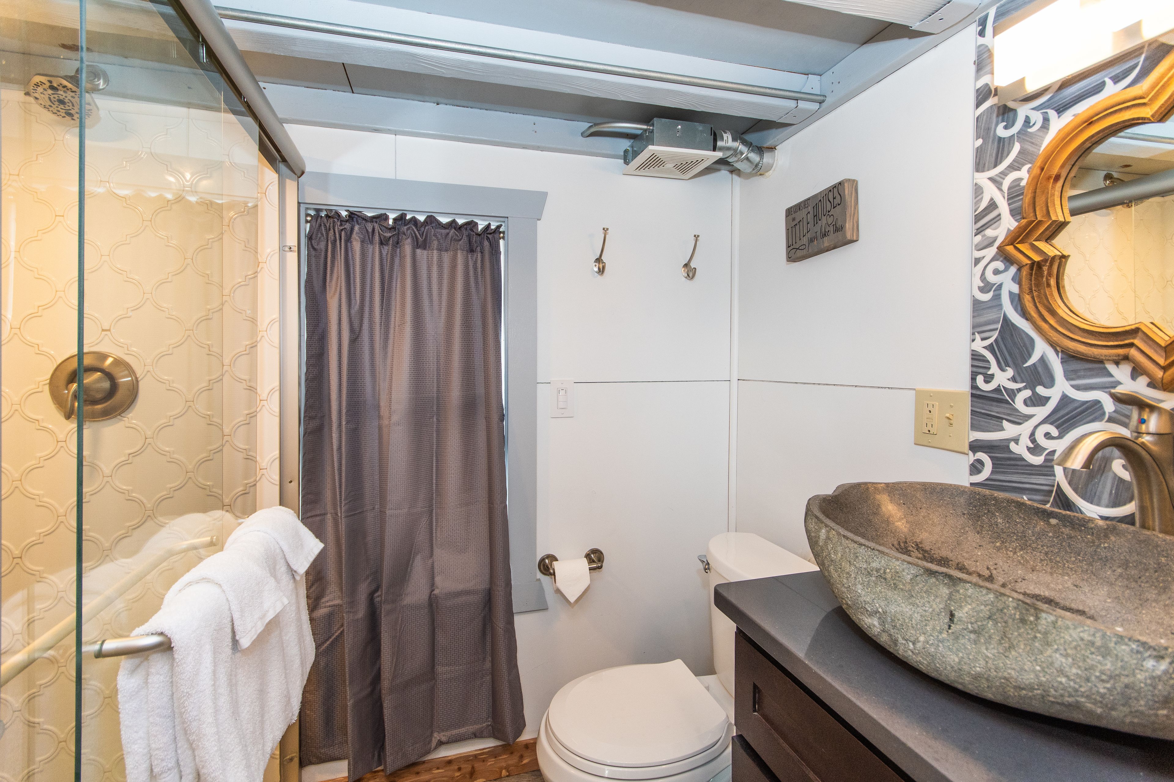Een badkamer met een wasbak van steen, een toilet, een douche met glazen deur en een handdoek aan een rek.