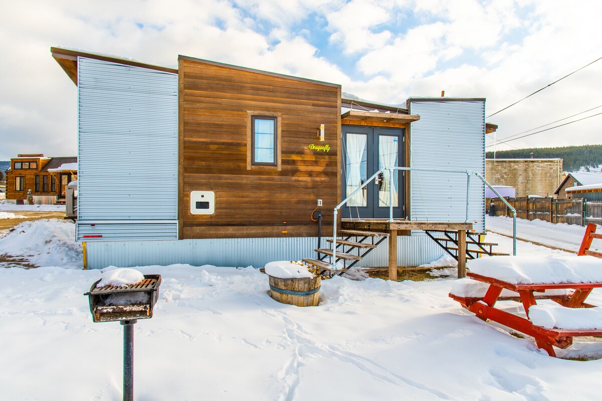 Une cabane en bois à l’extérieur bleu, avec une porte en bois et un petit porche doté d’un banc.