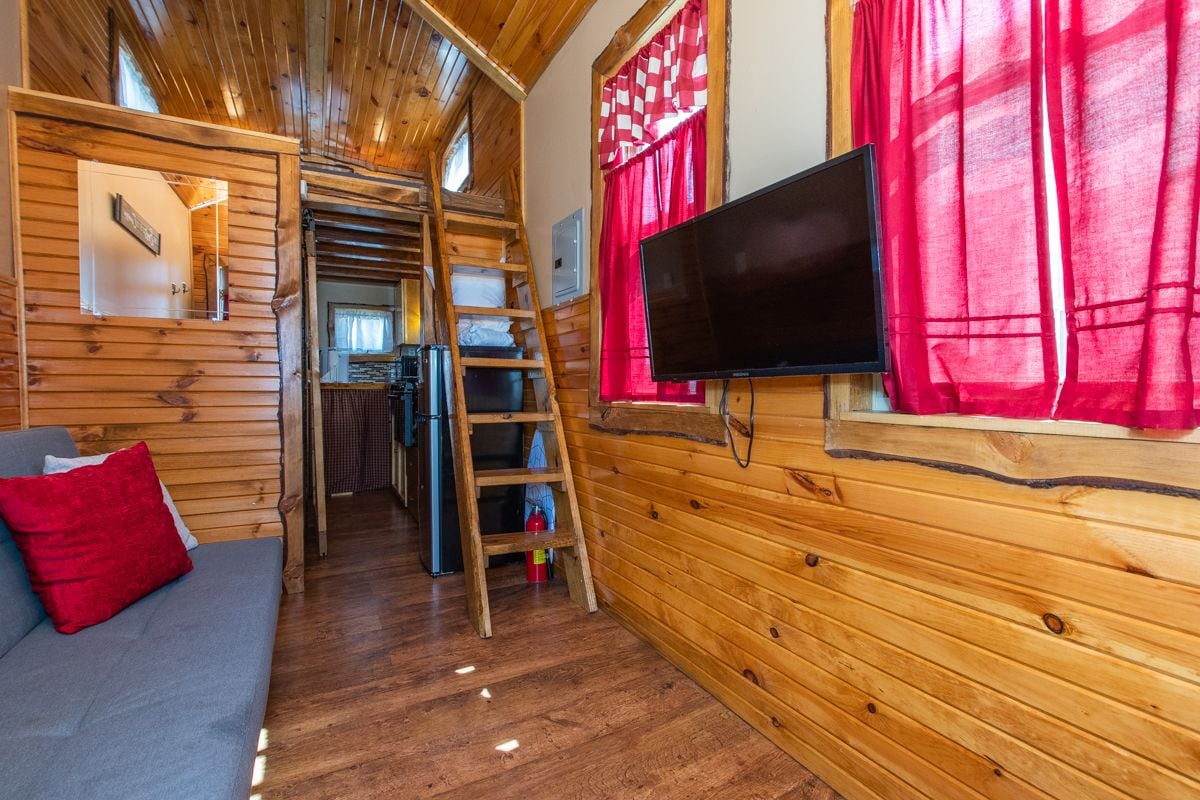A cozy cabin interior with a wooden interior, a sofa, a television, and a ladder leading to a loft area.