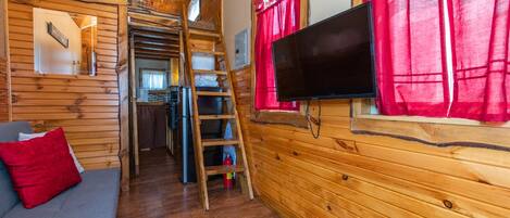 A cozy cabin interior with a wooden interior, a sofa, a television, and a ladder leading to a loft area.