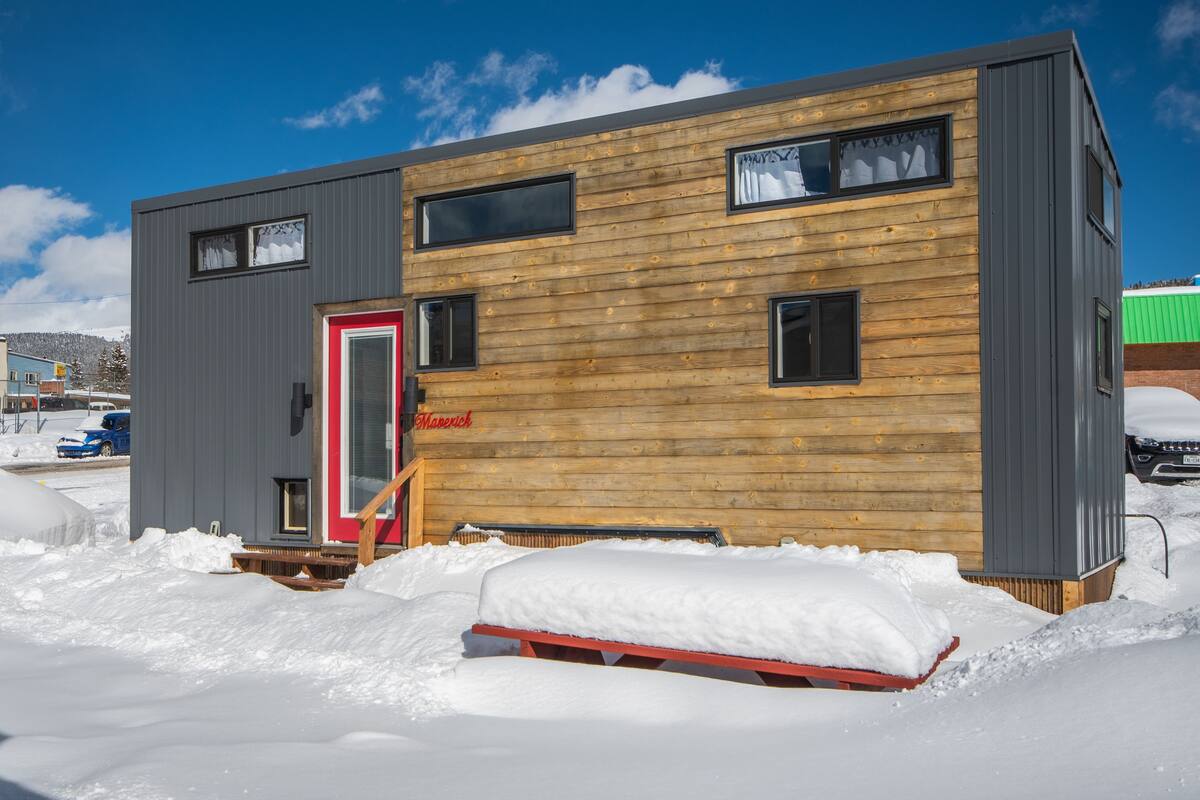 Une cabane moderne avec une façade en bois, une porte rouge et un petit porche.