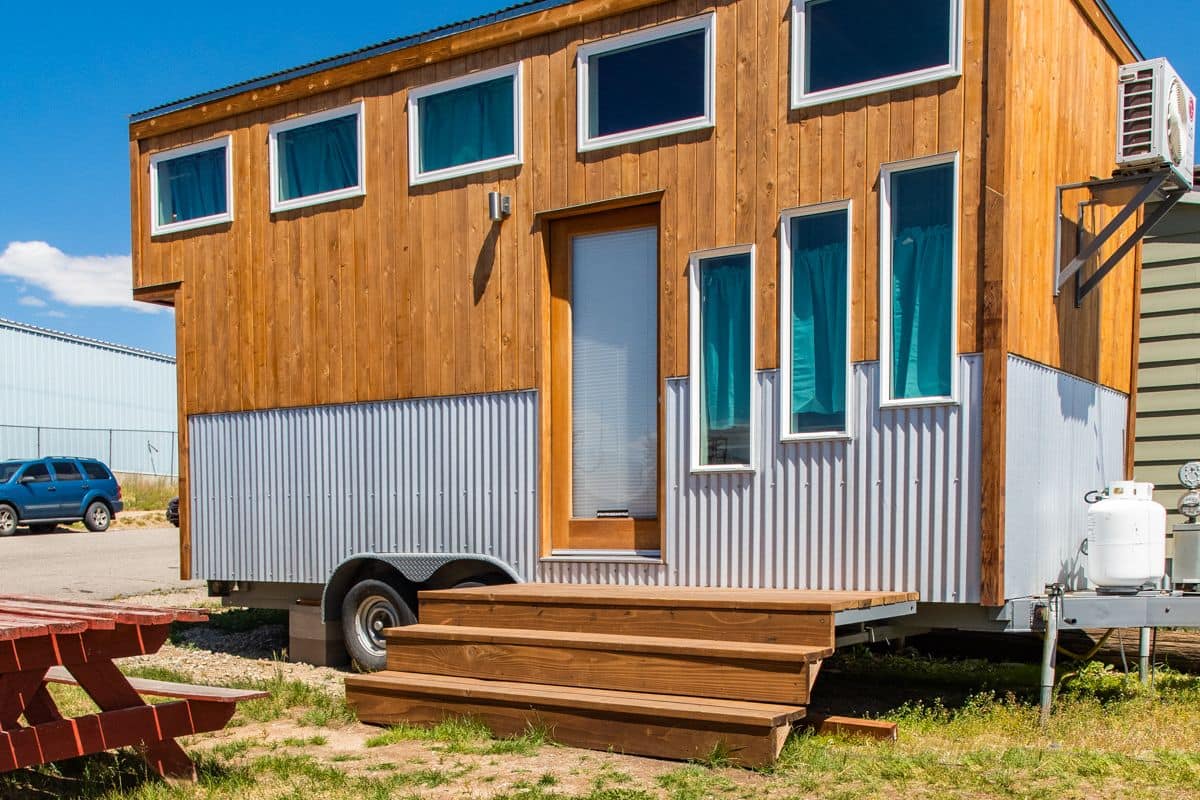 Une petite cabane en bois, dotée de plusieurs fenêtres et d’une porte, installée sur une remorque.
