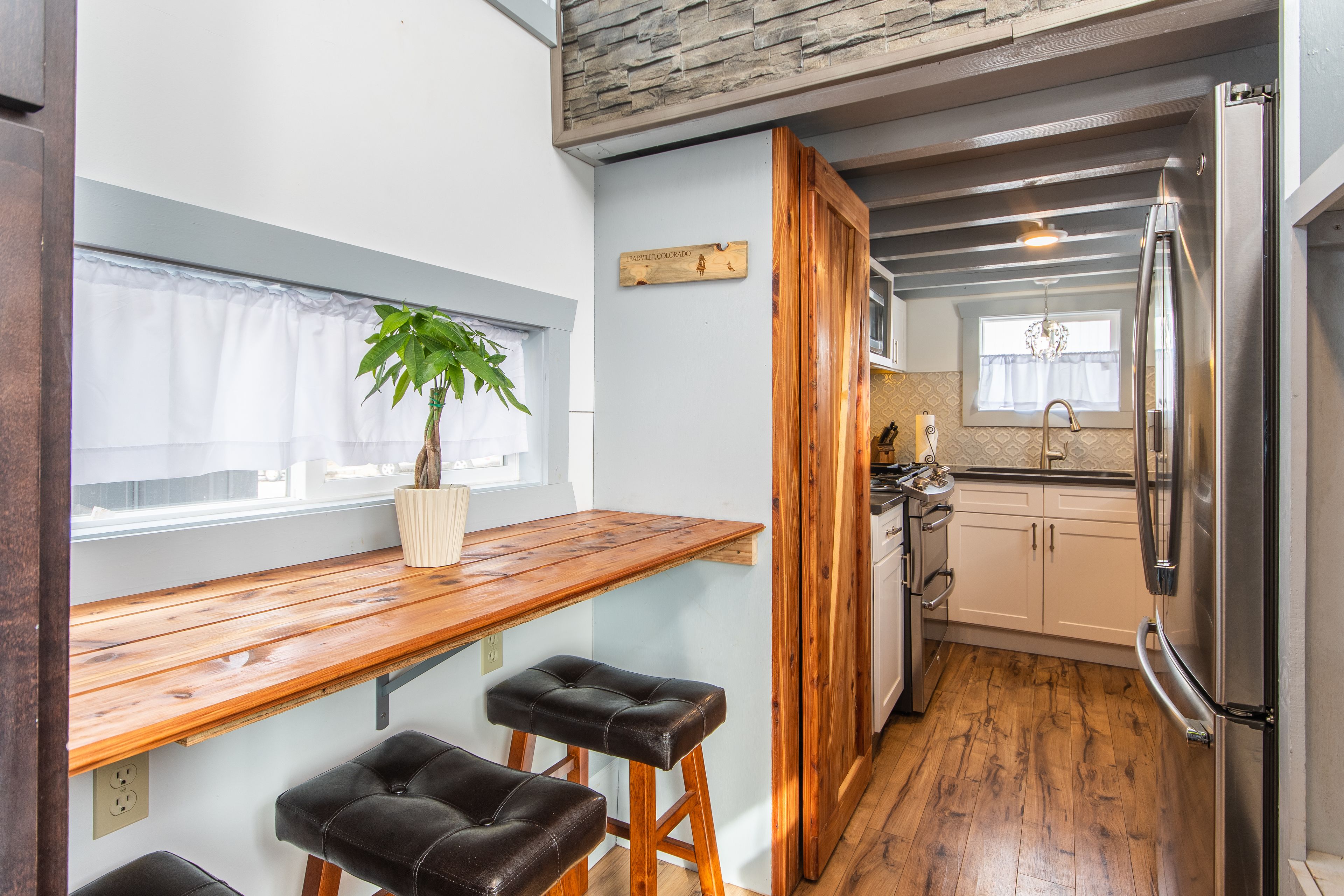 A kitchen with a wooden countertop, two stools, a refrigerator, and a window with a plant.