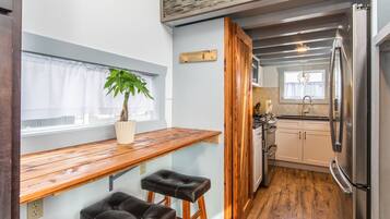 A kitchen with a wooden countertop, two stools, a refrigerator, and a window with a plant.