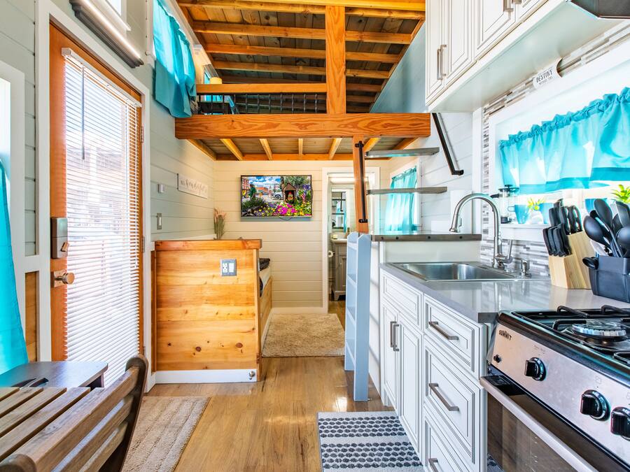 A kitchen with wooden beams, white cabinets, a stove, and a sink.