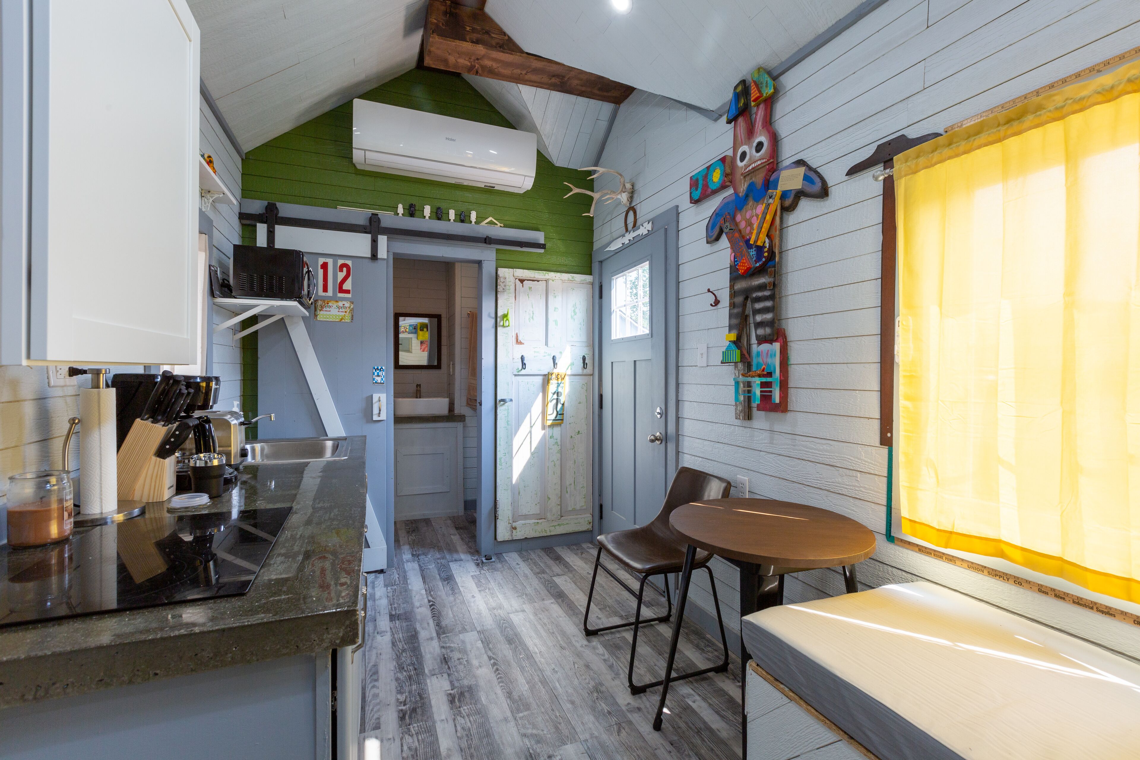 A kitchen with a wooden floor, a dining area with a bench, and a colorful wall decoration.