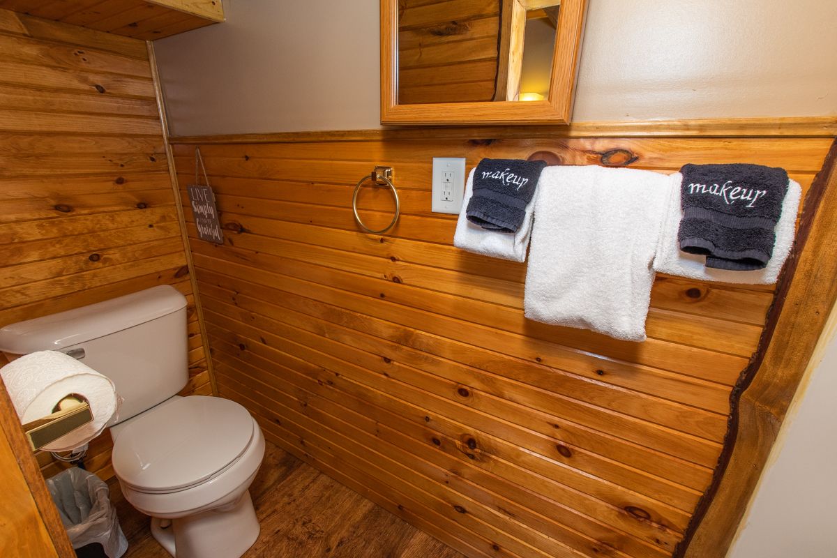 A wooden-paneled bathroom with a toilet, a hand towel, and a bath towel hanging on a towel rack.