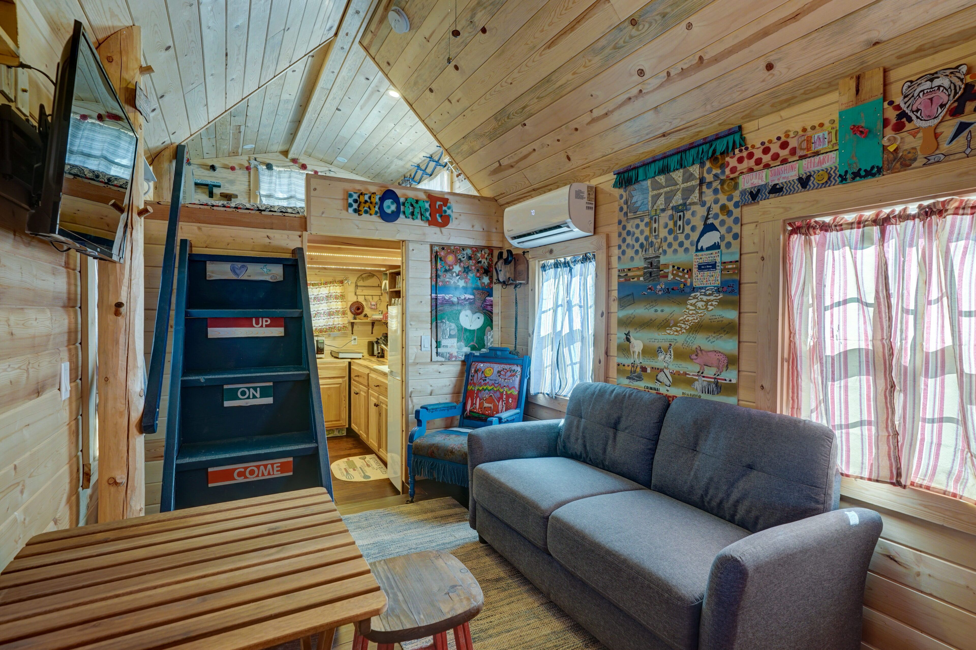 A cozy cabin interior with a wooden interior, a sofa, a table, and a ladder with 'UP' and 'COME' signs.