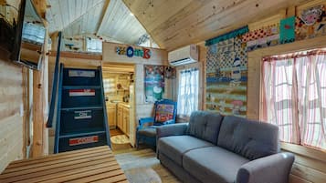 A cozy cabin interior with a wooden interior, a sofa, a table, and a ladder with 'UP' and 'COME' signs.