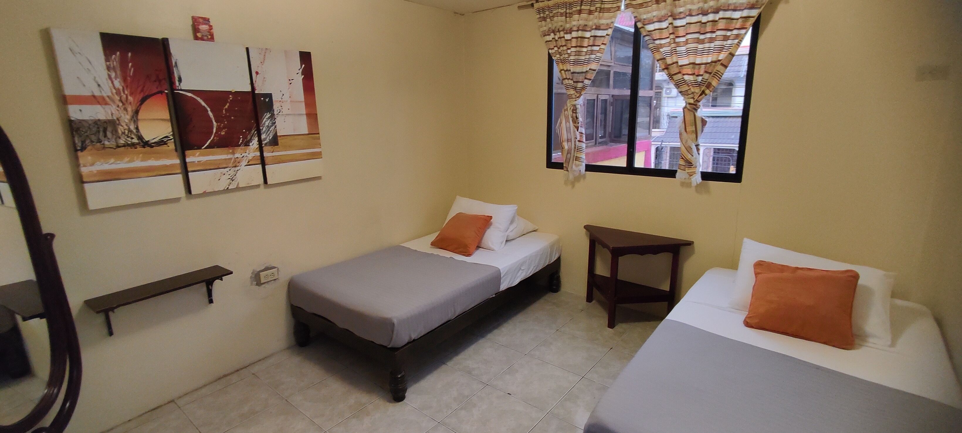 A small, well-lit room with two beds, a small table, and a shelf.