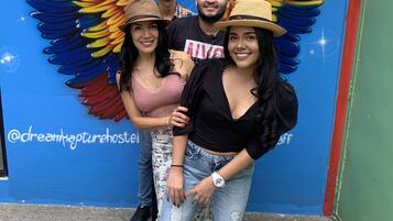 A group of people posing in front of a wall with a colorful mural featuring wings and a dreamcatcher symbol.