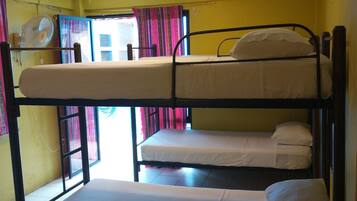 Un dormitorio con tres camas literas, un ventilador de techo y una ventana con cortinas.