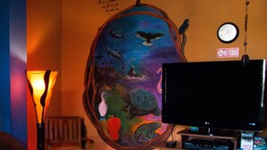 A room with a mural of a turtle, a clock, and a TV on a stand. - Dreamkapture Hostel (Guayaquil)