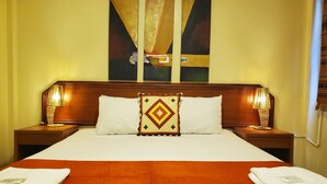 A hotel room with a large bed, two bedside lamps, a headboard, and two paintings on the wall. - Dreamkapture Hostel (Guayaquil)