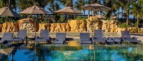 Una piscina al aire libre, sombrillas, sillones reclinables de piscina