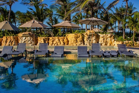 Una piscina al aire libre, sombrillas, sillones reclinables de piscina