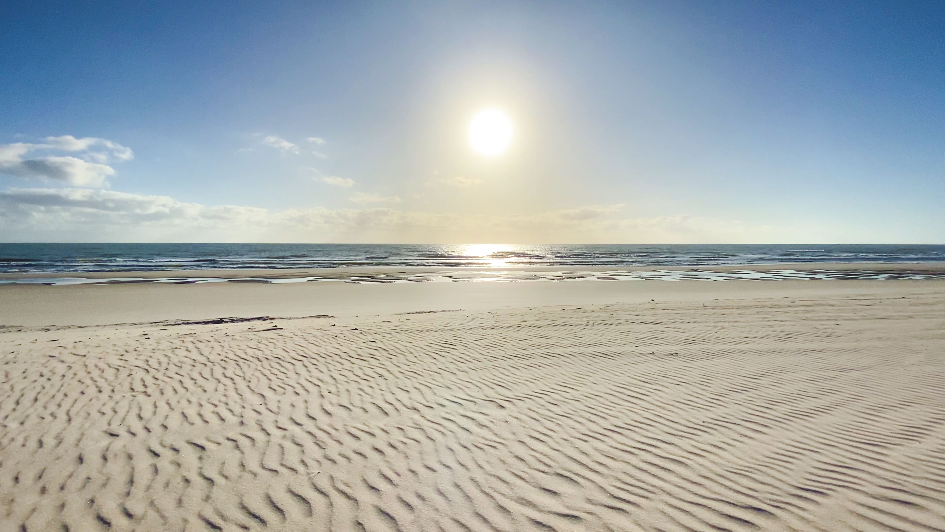 A beach with a clear sky and sunlight reflecting on the water.