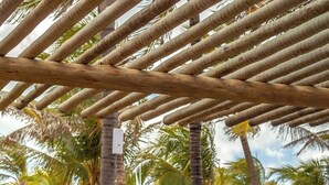 Eine Holzterrasse mit Essbereich mit Blick auf einen Pool, umgeben von Palmen und Strand.