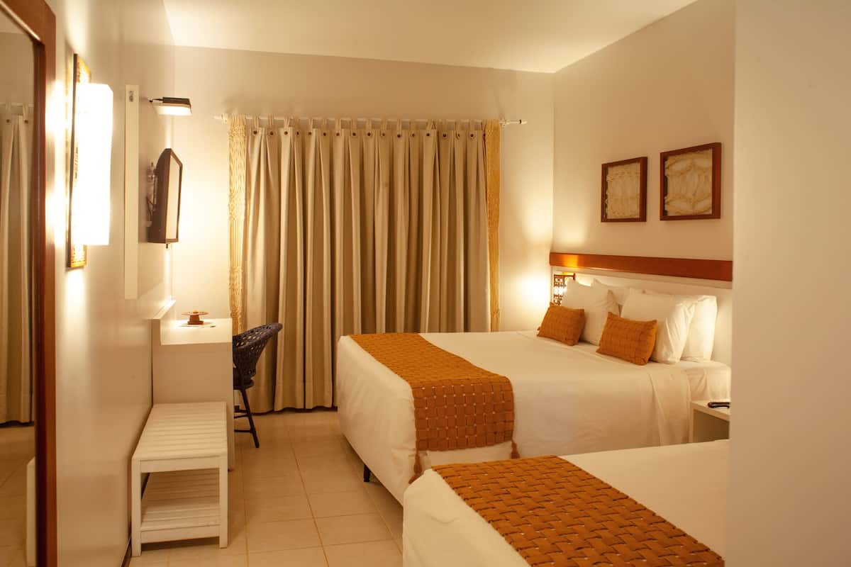 A hotel room with two beds, a desk, a chair, a lamp, and a curtain.