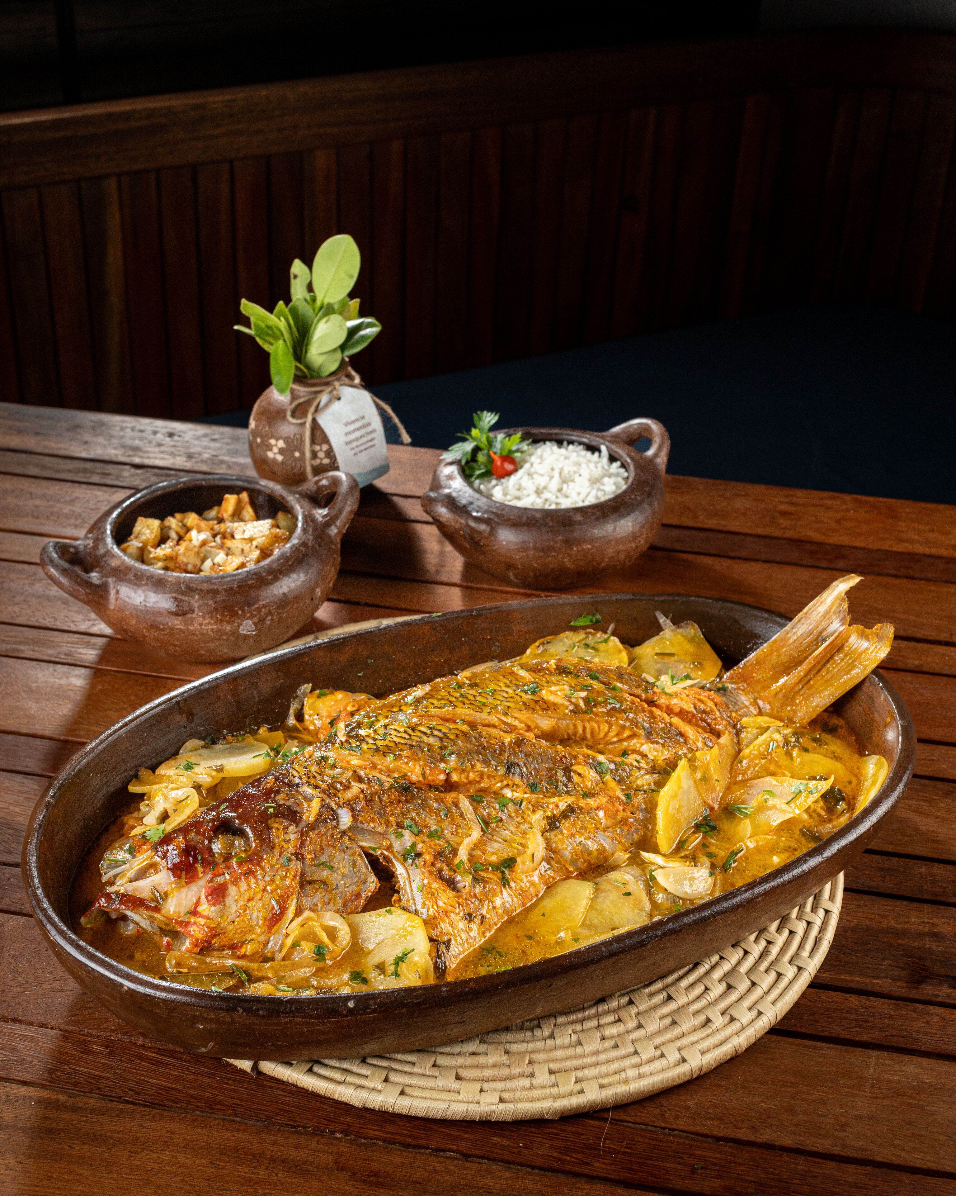 A wooden table with a large fish dish, a small bowl of rice, and a small bowl of sauce.