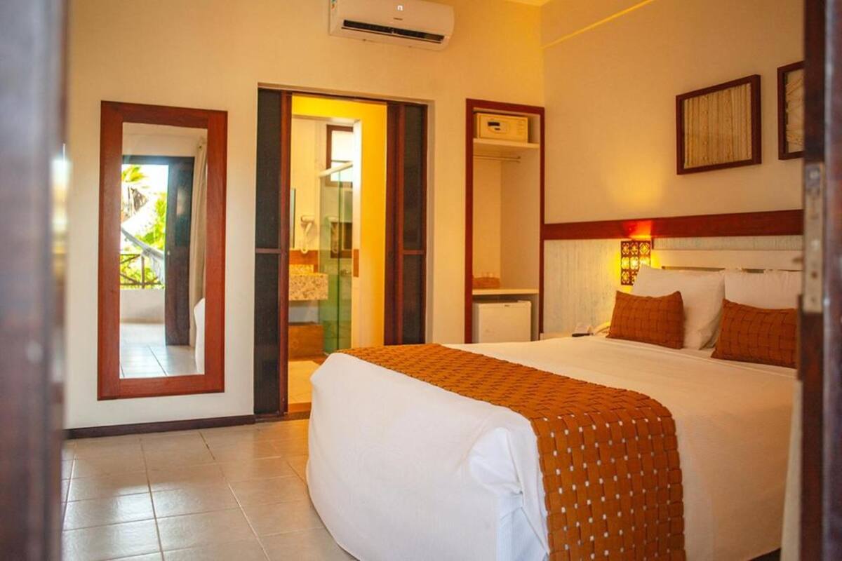 A hotel room with a bed, a wardrobe, an air conditioning unit, and a door leading to an outdoor area.