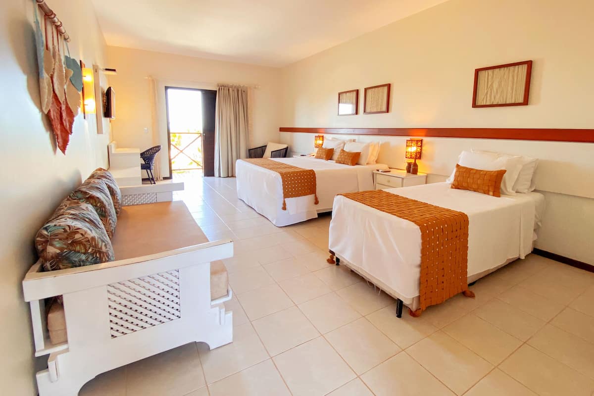 A hotel room with two beds, a sofa, a small table, and a view of the outside.