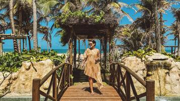 A wooden bridge leading to a gazebo surrounded by palm trees and a clear blue sky.