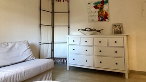 Ein Zimmer mit einem weißen Sofa, einem weißen Schminktisch mit Schubladen, einem Bild an der Wand und einem Fenster mit Vorhang.